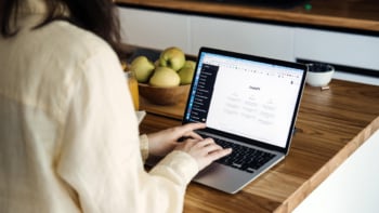 Donna che utilizza ChatGPT su un laptop in casa, scrivendo contenuti digitali a un tavolo di legno