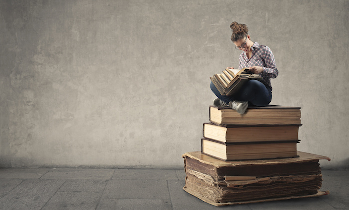 Young woman reading while sitting on a pile of books