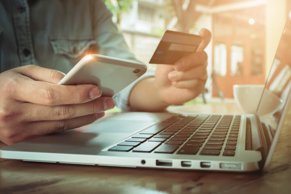 homem em frente a laptop com smartphone e cartao de credito em maos fazendo compras em e-commerce