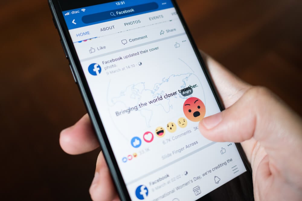 mao masculina segurando smartphone com post do aplicativo facebook em tela