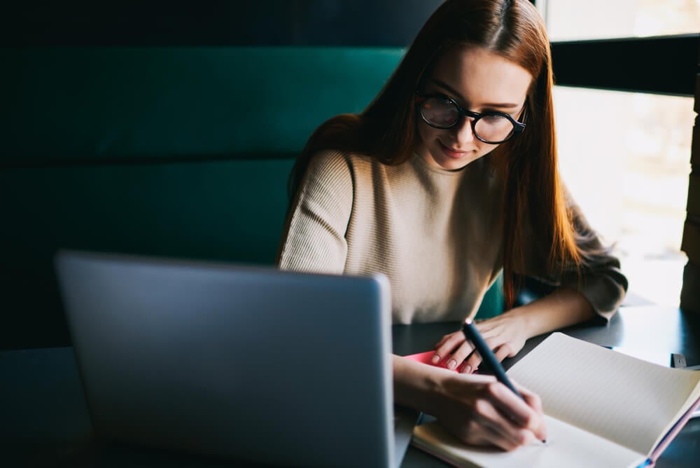 moça fazendo anotações ao lado do laptop