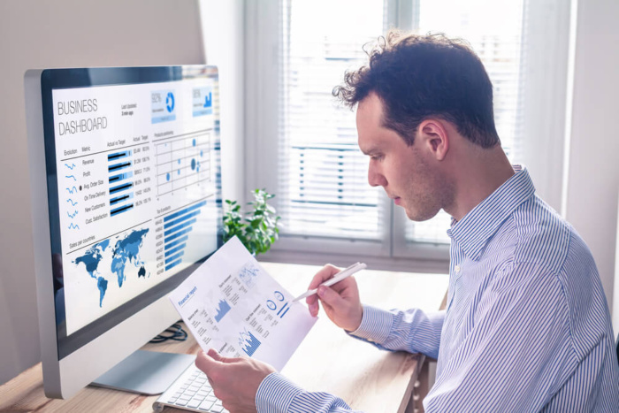 homem segurando papel em frente a computador, analisando o ticket médio