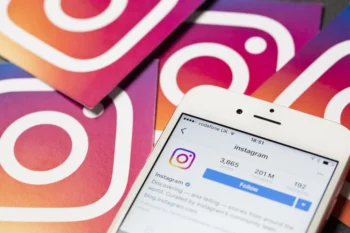 smartphone com aplicativo instagram em tela e logo de instagram ao fundo